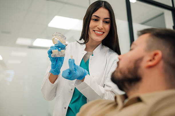 Female dentist explaining to male patient the benefits of dental implants using a model of a jaw